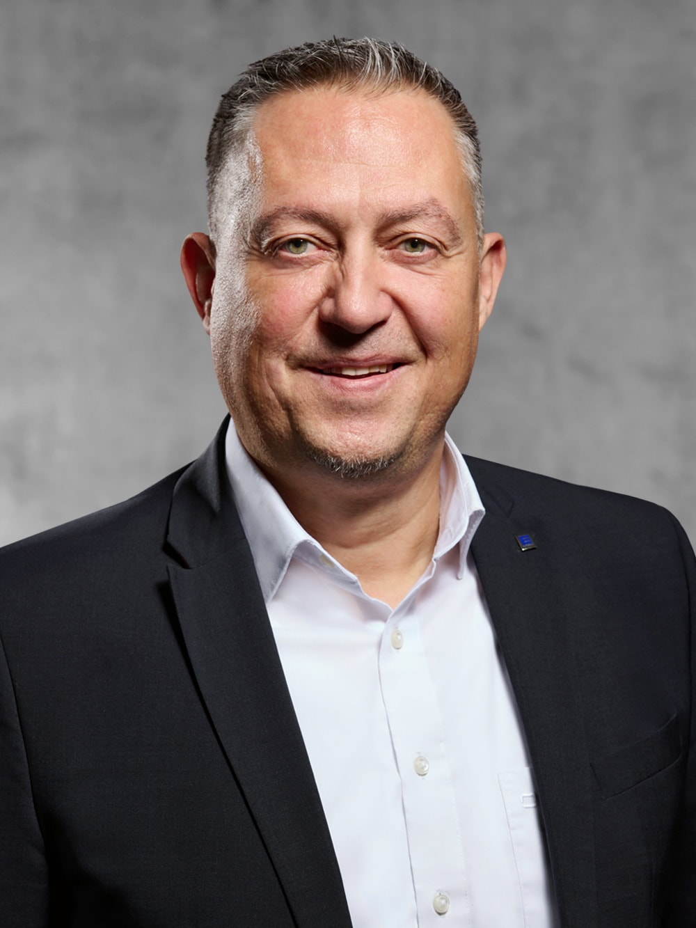 Portrait von Dirk Dombrowsky. Lächelnder Mann mittleren Alters mit graumeliertem Kurzhaarschnitt trägt ein schwarzes Jackett