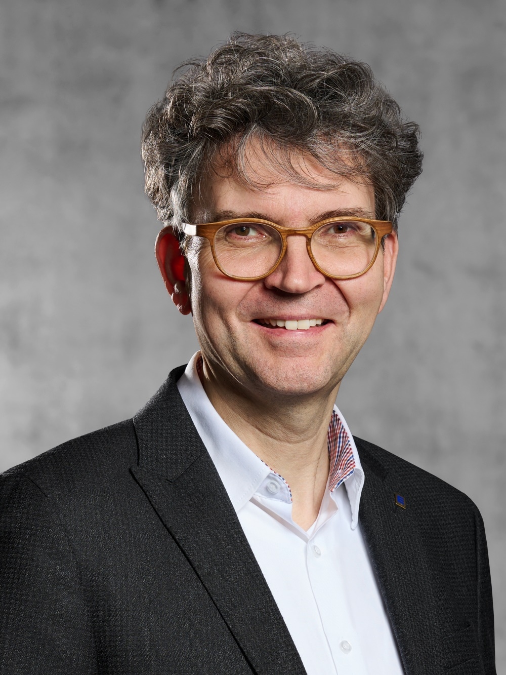 Portrait von Sebastian Gottschalk. Mann mit graumeliertem welligem Deckhaar und Brille in weißem Hemd und Jackett. 