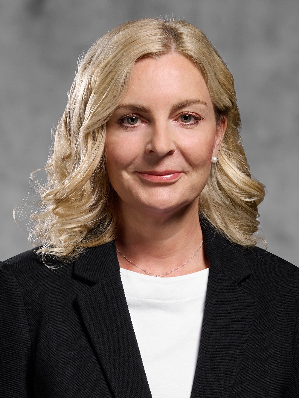 Portrait von Bianka Janssen. Lächelnde Frau mit schulterlangem blondem Haar, in weißem Shirt und schwarzem Blazer.