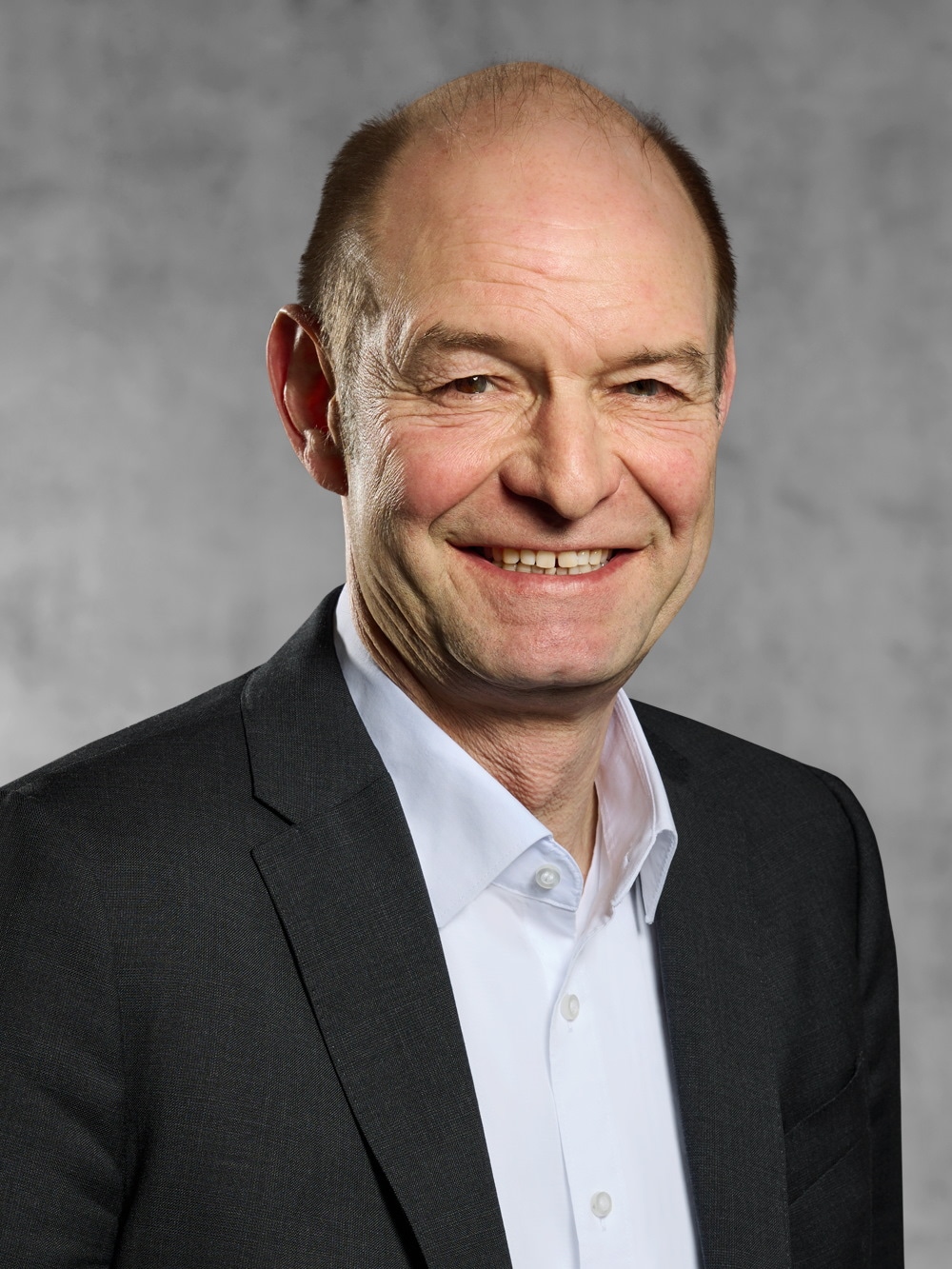 Portrait von Roger Otte. Lächelnder Mann mit kurzem dunklem Haar, trägt ein weißes Hemd und ein schwarzes Jackett.