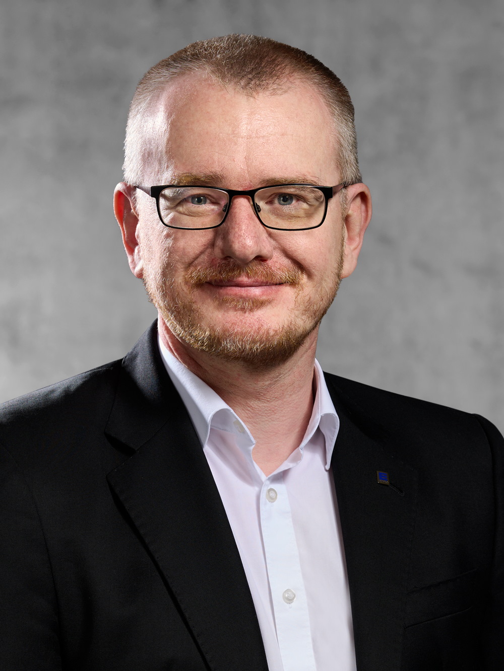 Portrait von Markus Schäfer. Mann mit kurzem dunklem Haar und Bart, trägt Brille, ein weißes Hemd und ein schwarzes Jackett.