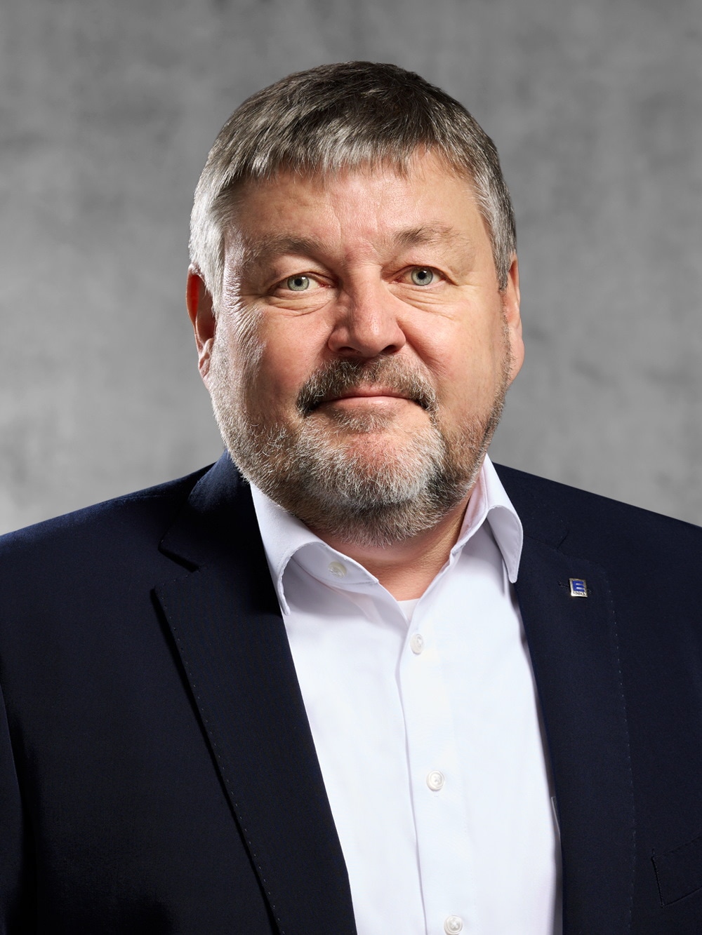 Portrait von Uwe Schatto. Mann mit kurzem graumeliertem Haar und Bart, weißes Hemd und schwarzes Jackett