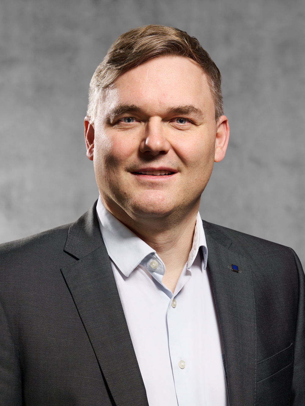 Portrait von Ralf Stumpf. Mann mit blondem kurzem Haar,  lächelt, trägt weißes Hemd und graues Jackett