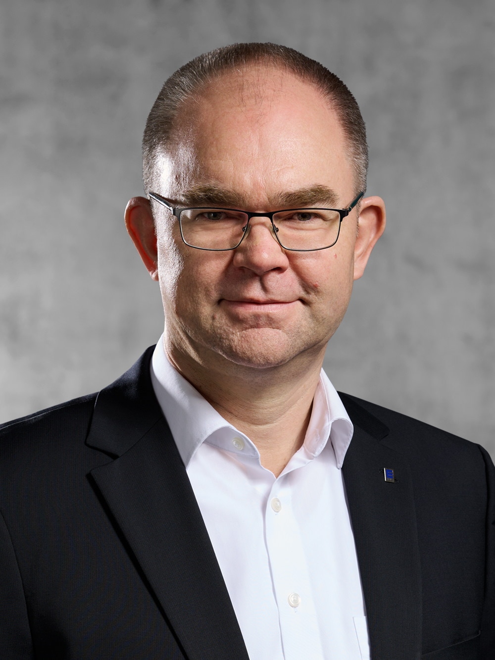 Portrait von Jörn Wagner. Mann mit kurzem dunklen Haar, trägt Brille, weißes Hemd und schwarzes Jackett