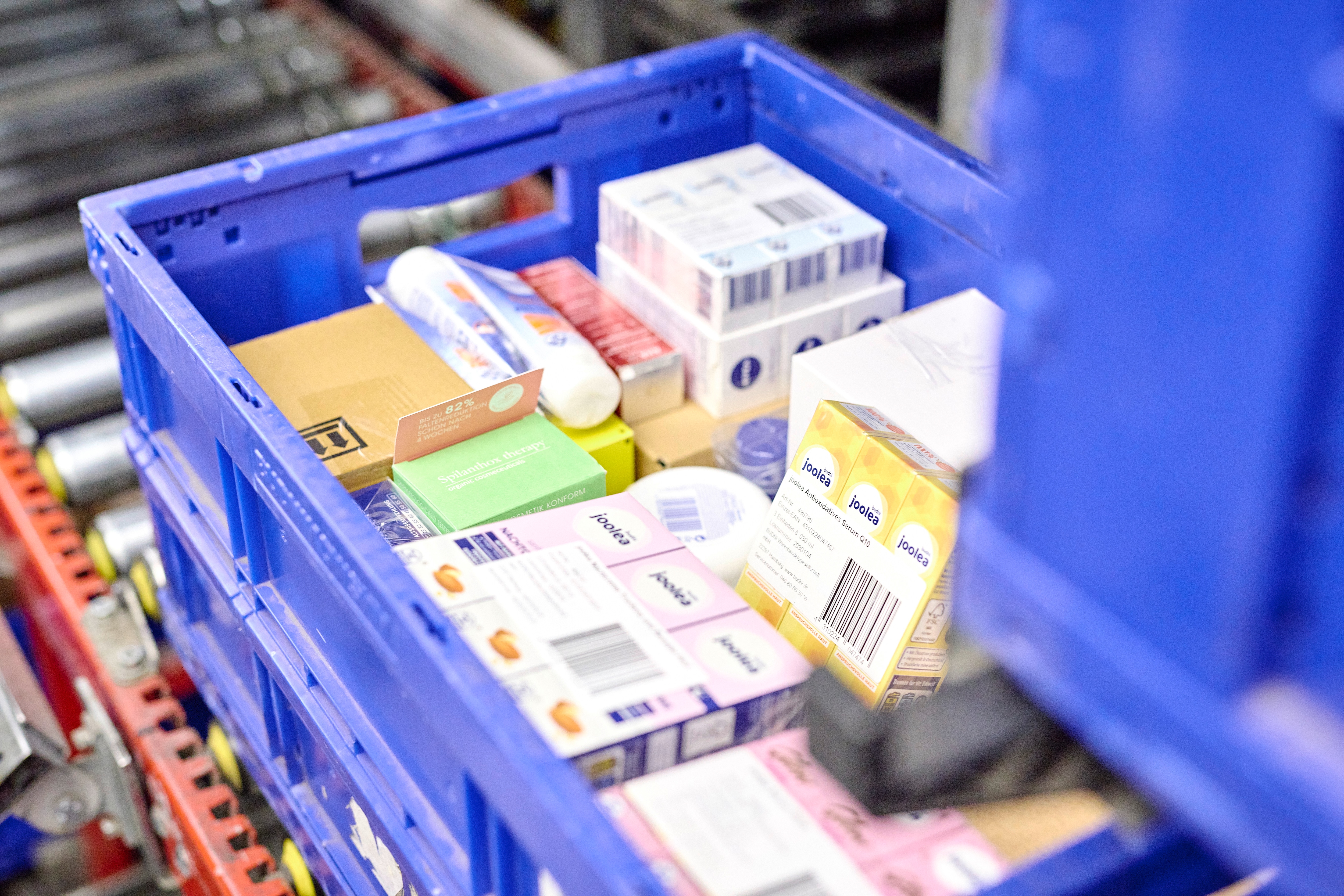 Blaue Kunststoffkiste mit verschiedenen verpackten Produkten auf einem Förderband