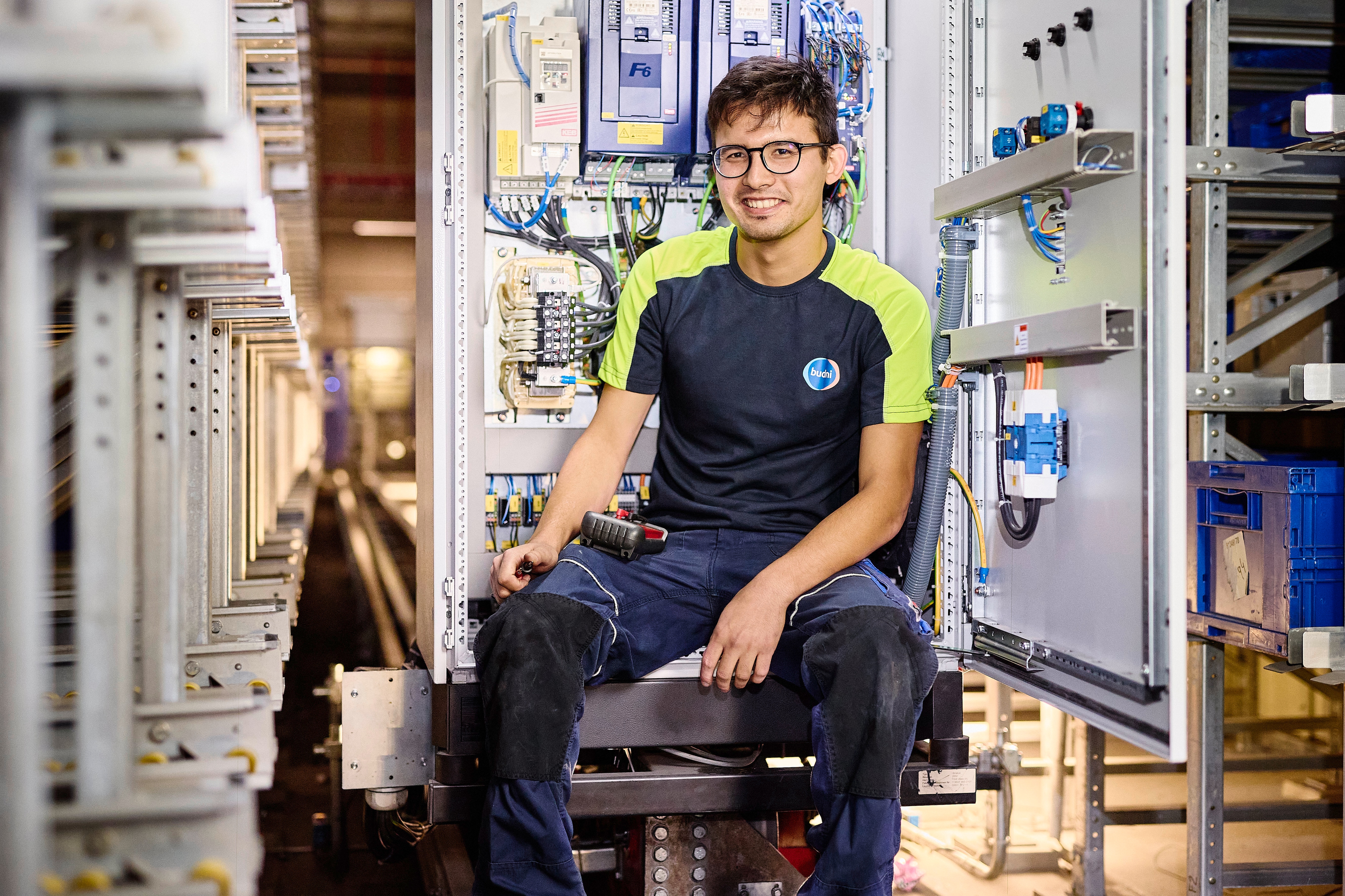 BUDNI Techniker Amir Shivzad sitzt vor geöffnetem Schaltschrank mit Kabeln, Schaltern und elektronischen Komponenten