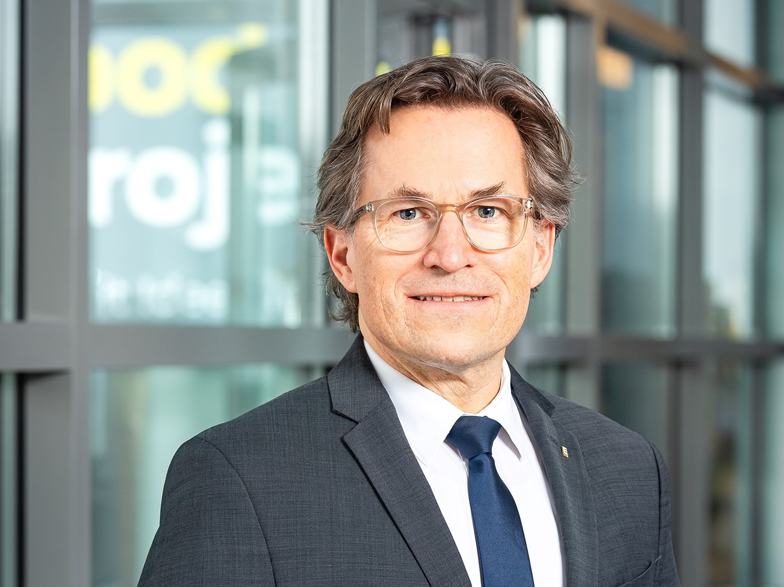 Portraitbild von Markus Mosa. Er trägt einen grauen Anzug mit weißem Hemd und dunkelblauer Krawatte. 