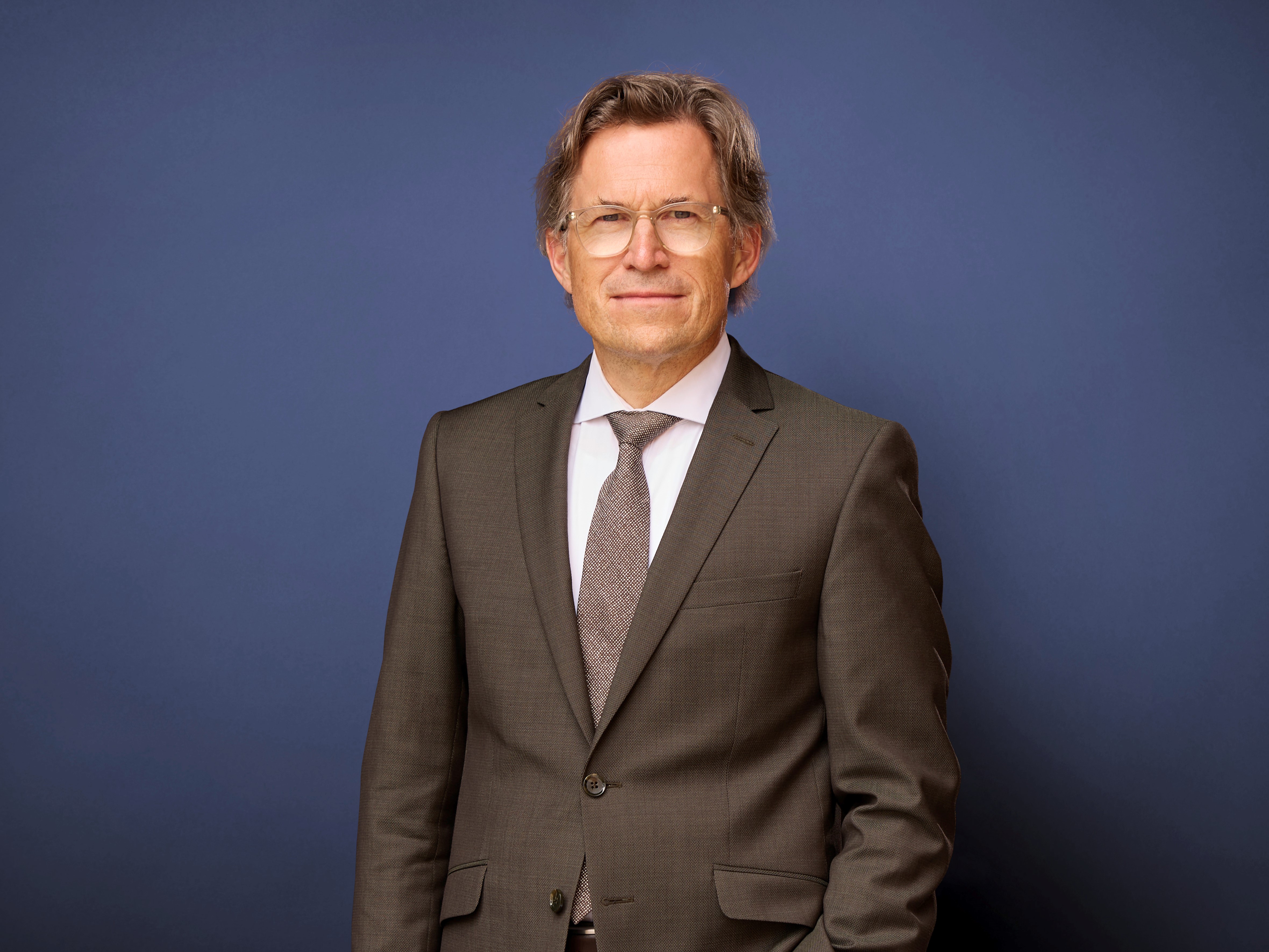 Portrait von Markus Mosa vor neutralem Hintergrund. Er trägt ein braunes Sakko.