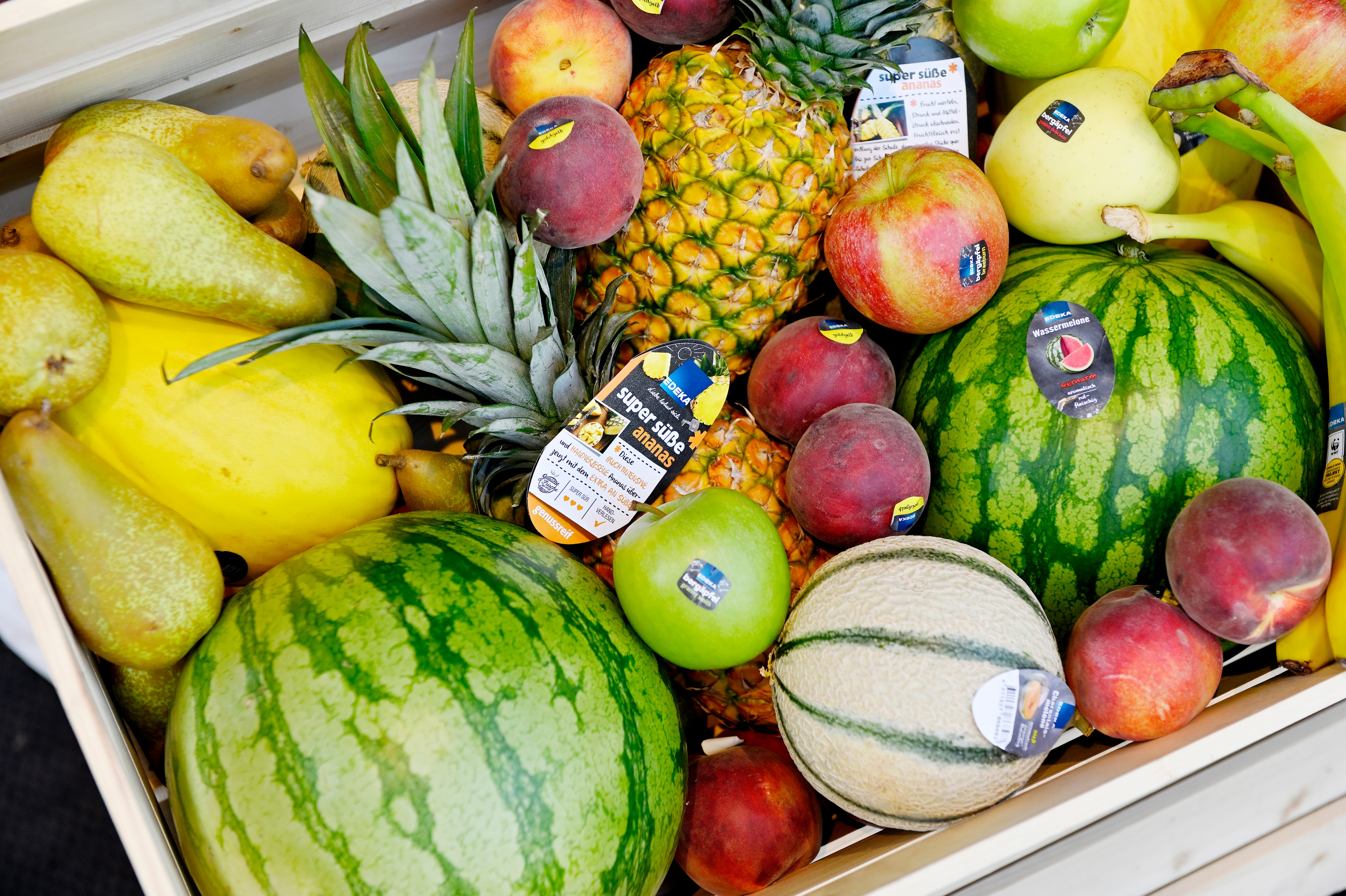 Ein großes Holztablett voller Obst, darunter Birnen, Melonen, Nektarinen, Äpfel, Bananen und Ananas.