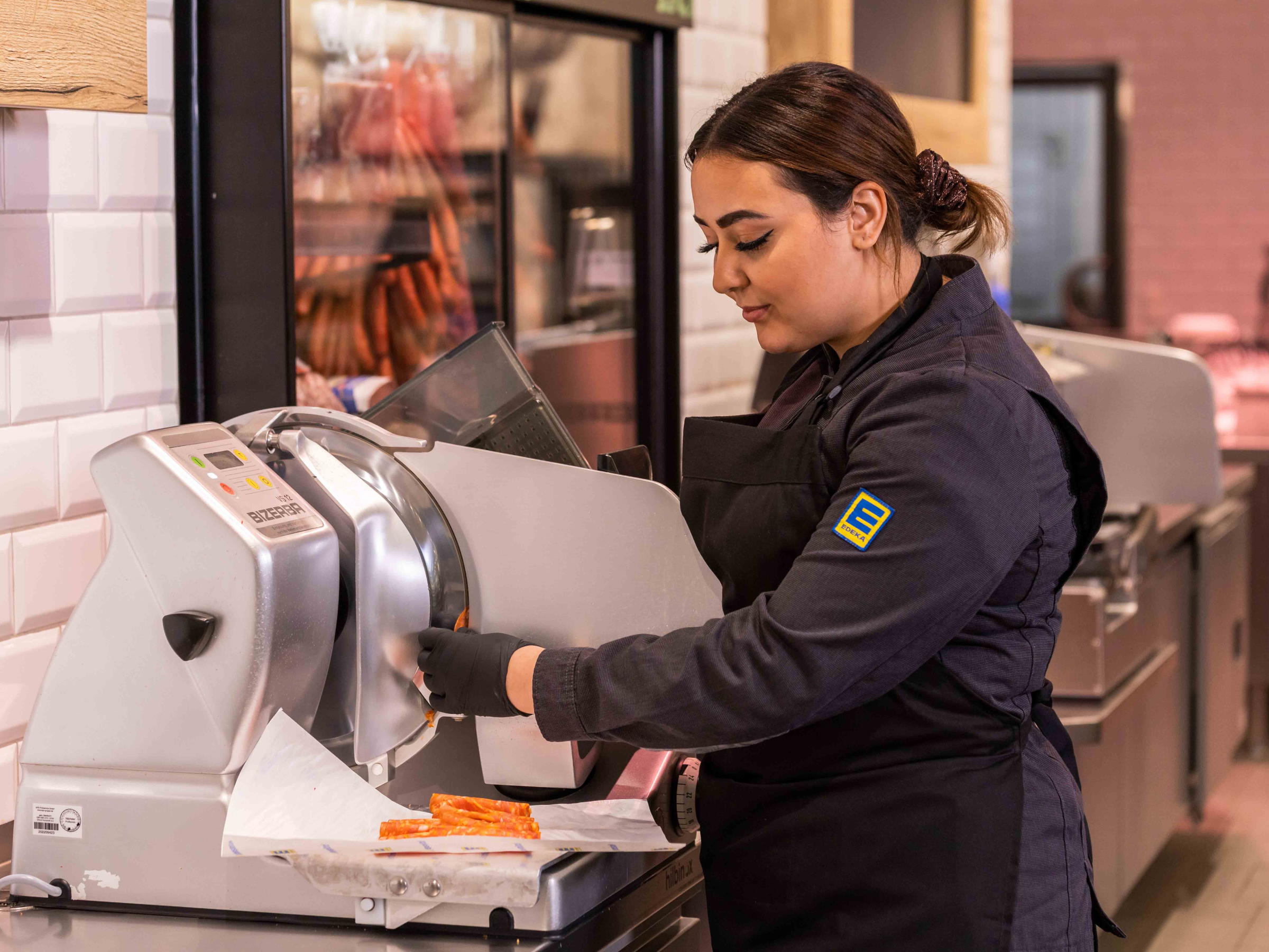 Junge Frau scheidet in der Bedienungsabteilung Wurst mit der Aufschnittmaschine in Scheiben.