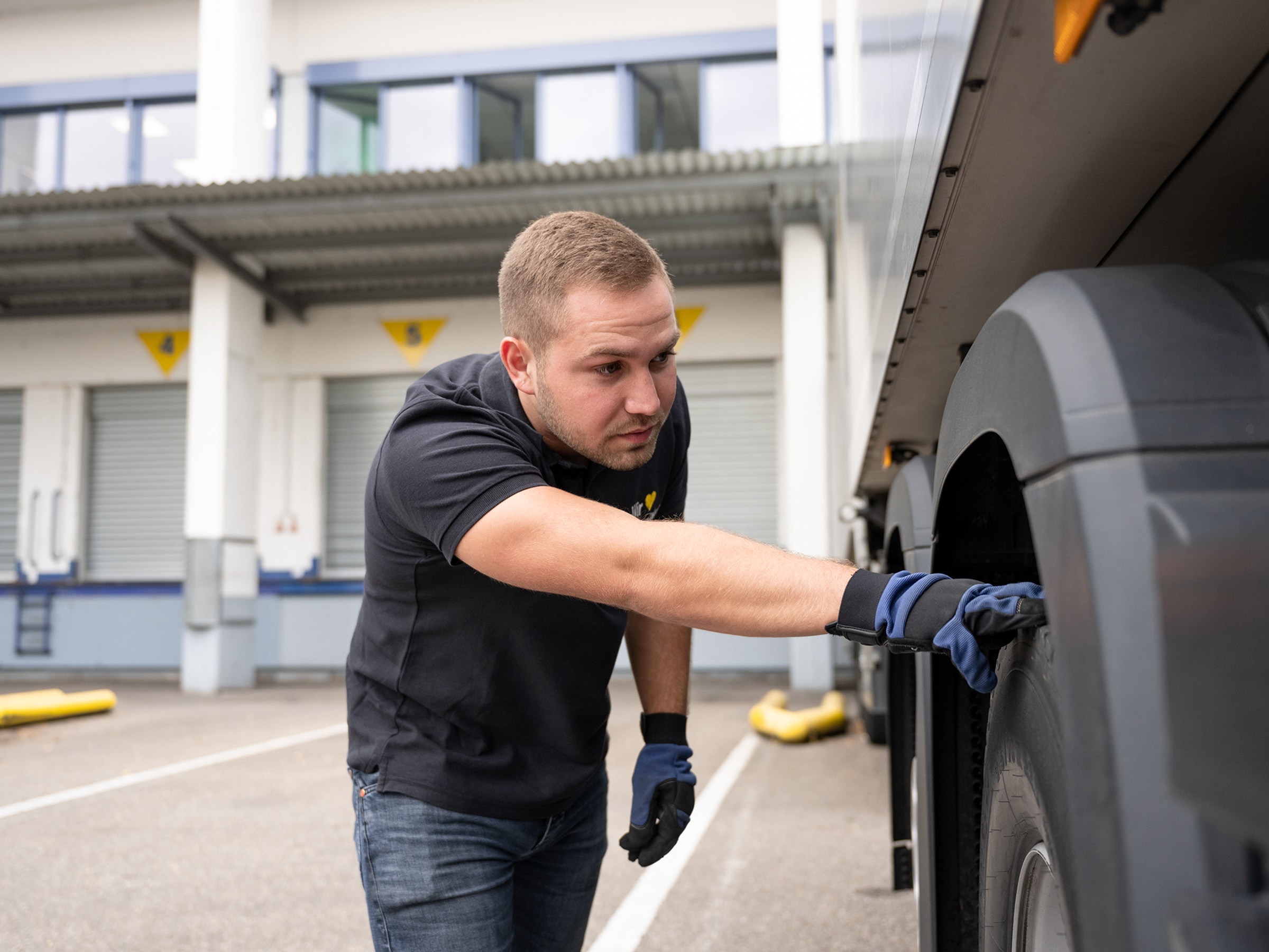Junger Mann hat seine Hand auf einem Lkw-Reifen und schaut in den Radkasten des Lkws.