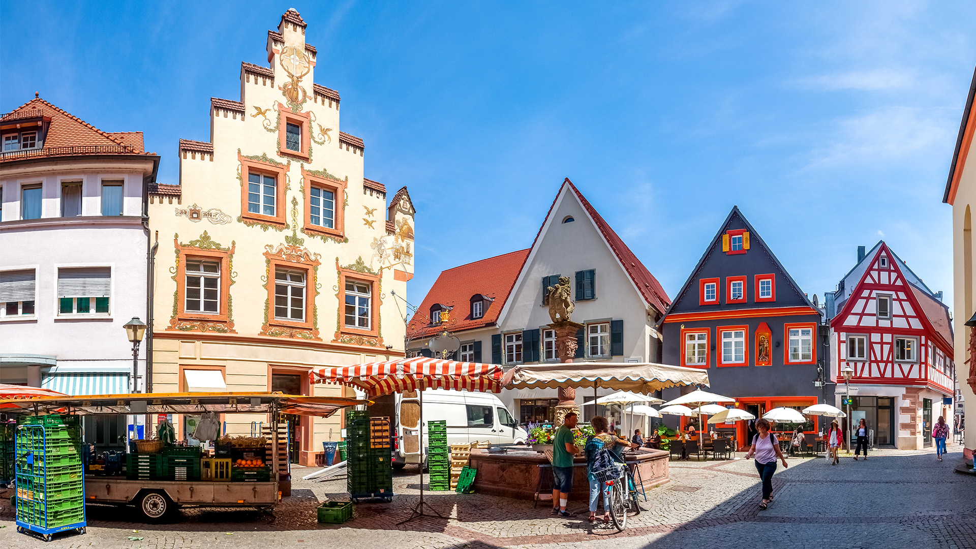 Marktstände stehen auf einem Platz in der Stadt, umgeben von schönen historischen Häusern und blauem Himmel.