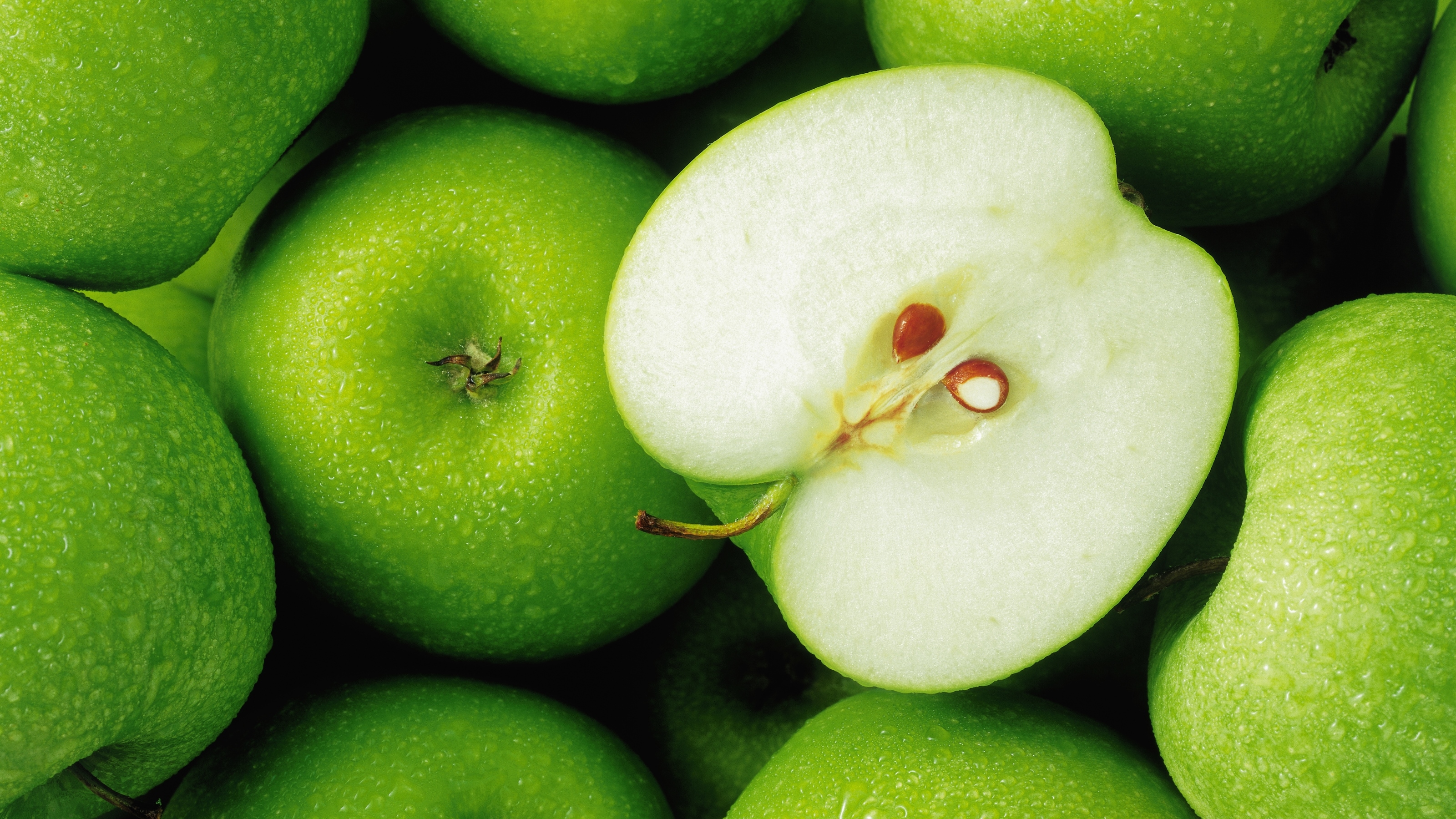 Grüne frische Äpfel mit kleinen Wassertropfen, einer davon ist zur Hälfte aufgeschnitten.