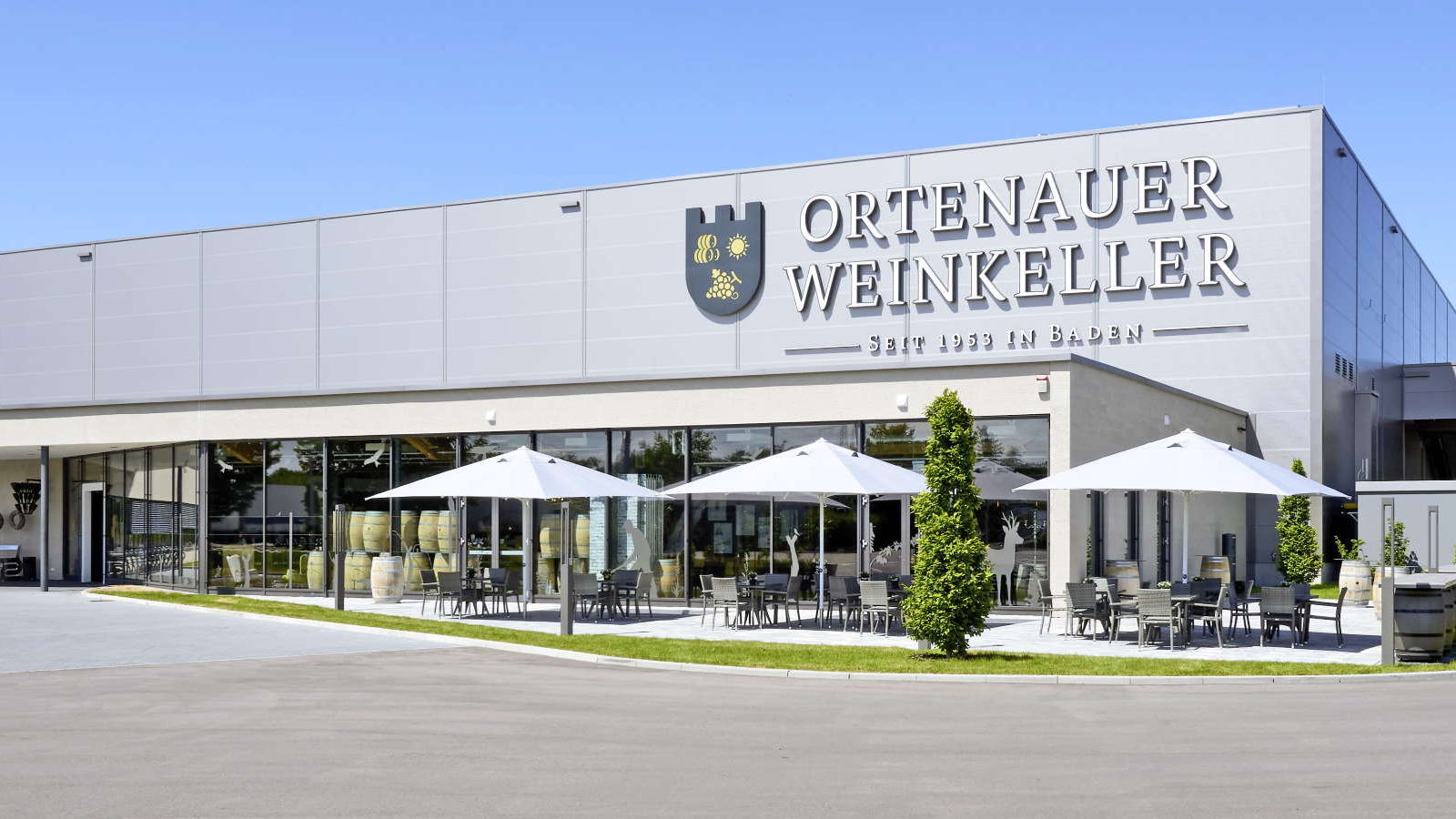 Außenansicht der Produktionsstätte Ortenauer Weinkeller, davor Sonnenschirme mit Tischen und Stühlen darunter