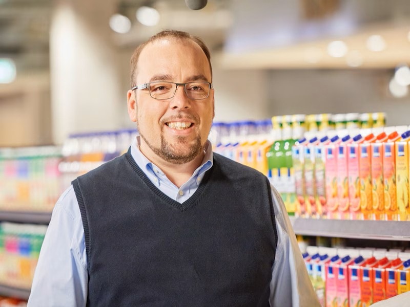 Kaufmann Christos Didis steht im Gang eines Supermarktes mit gut sortierten Regalen.