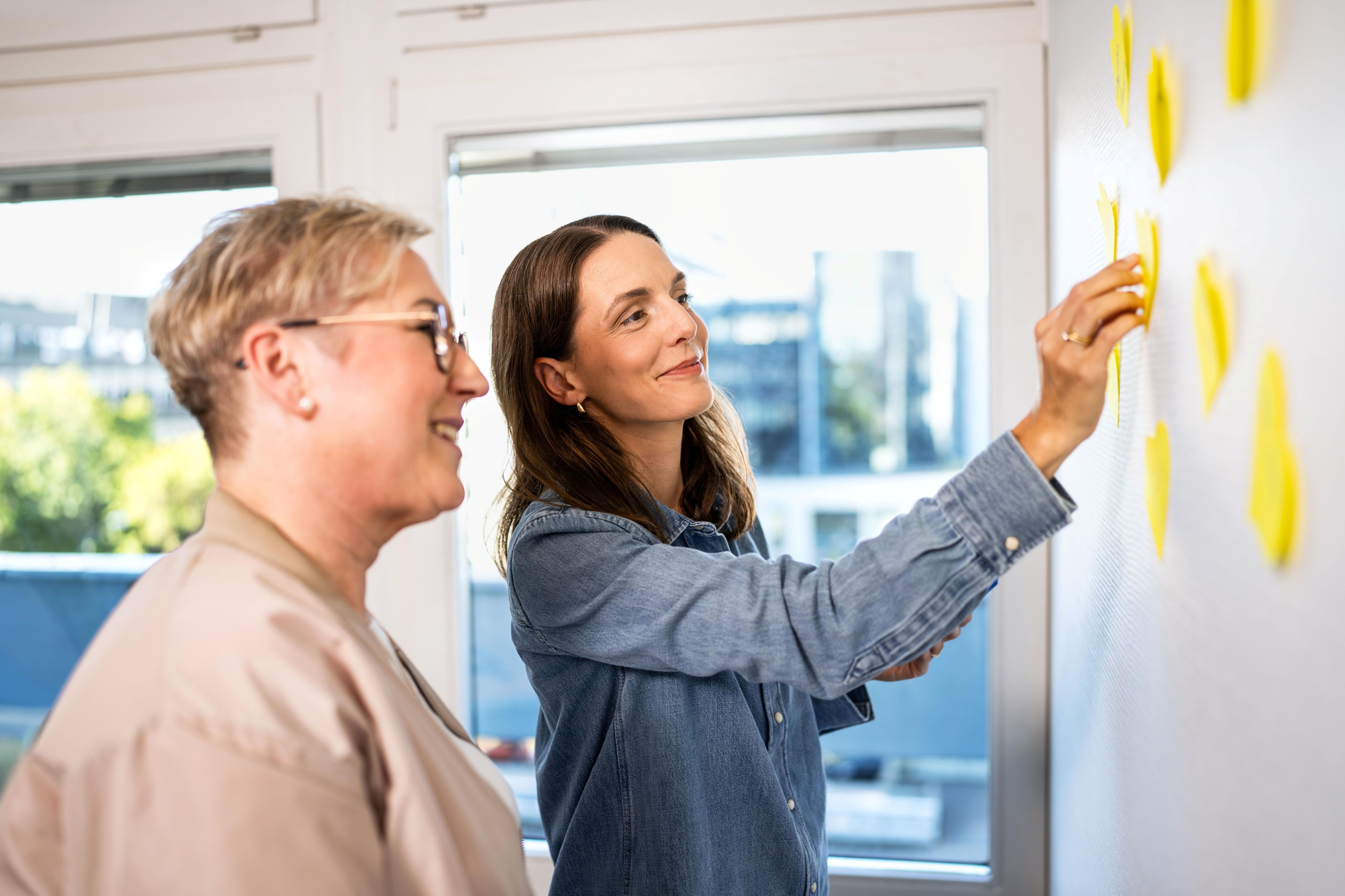 Kolleginnen kleben Postits an eine Wand und sprechen darüber